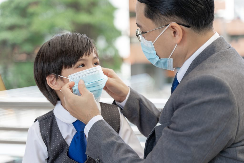 Seorang ayah memakaikan masker pada anaknya yang akan berangkat sekolah sebagai tindakan preventif dalam melawan polusi udara.